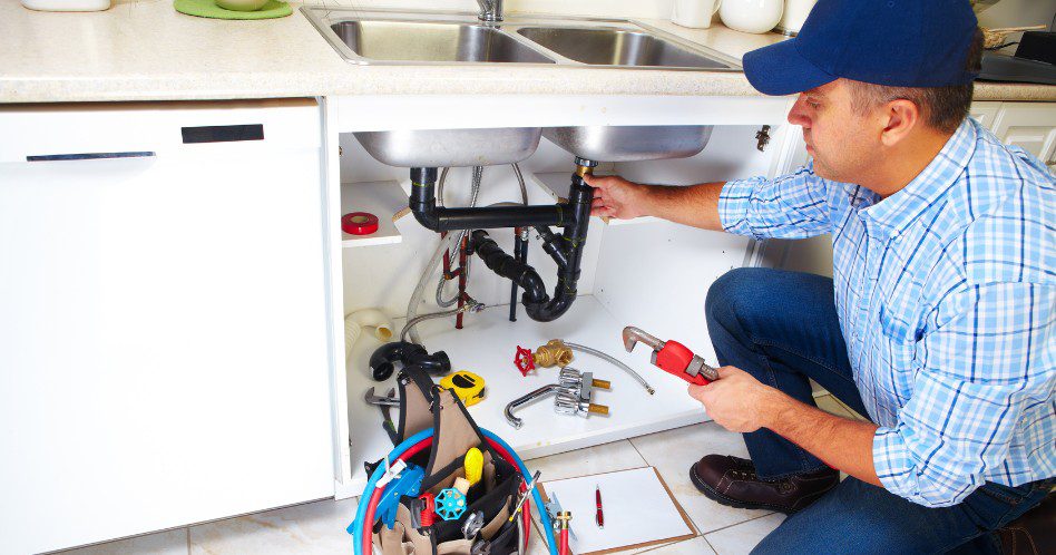 Plumber fixing sink pipes in a kitchen